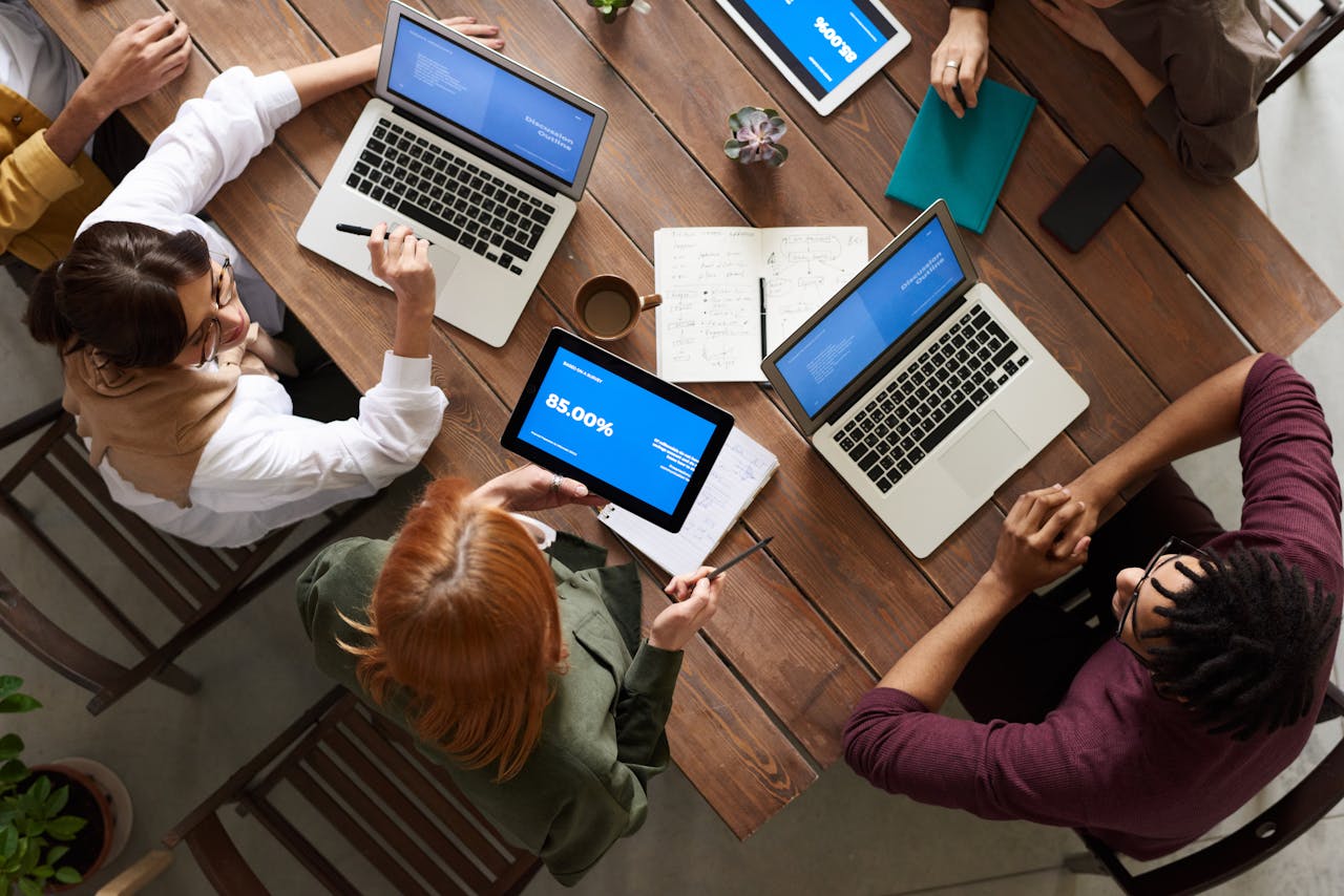 ours-journey Diverse team discussing business strategies with laptops and tablets at a wooden table.